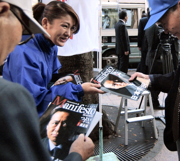 街頭演説会場で配られるマニフェストの冊子を手にする有権者たち（Ｃ）共同通信社
