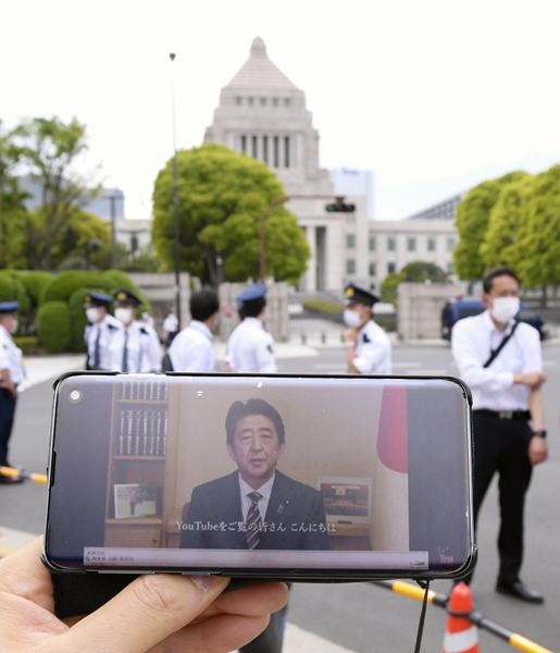 3日、スマートフォンの画面に映し出された、改憲派の会合に寄せられた安倍首相のビデオメッセージ。奥は国会議事堂（Ｃ）共同通信社