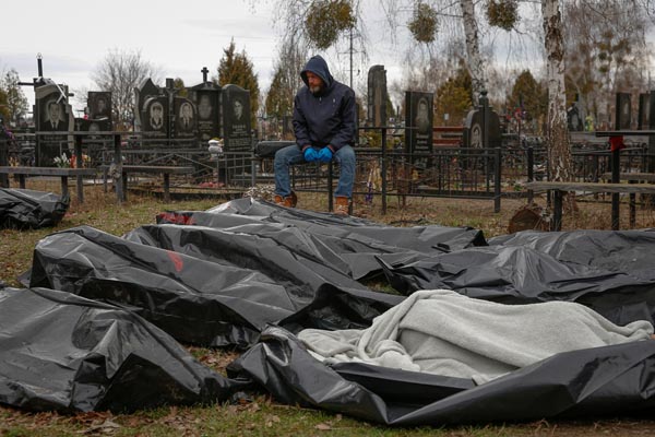 路上から墓地に集められた市民の遺体の側に座り込む葬儀従業員（6日、ブチャの町）／（Ｃ）ロイター