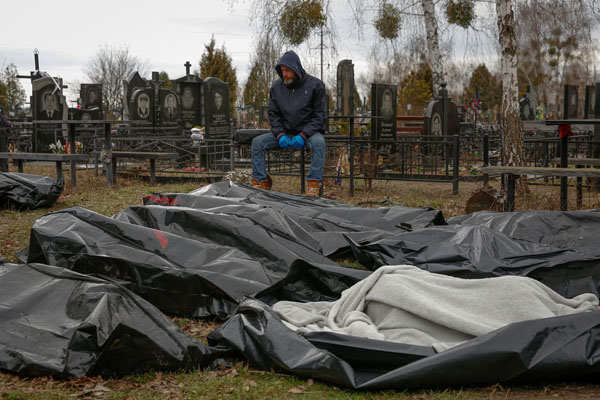 路上から墓地に集められた市民の遺体の側で座り込む葬儀従業員（6日、ブチャの町）／（Ｃ）ロイター