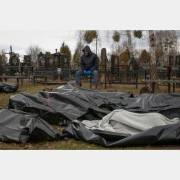 路上から墓地に集められた市民の遺体の側で座り込む葬儀従業員（6日、ブチャの町）／（Ｃ）ロイター
