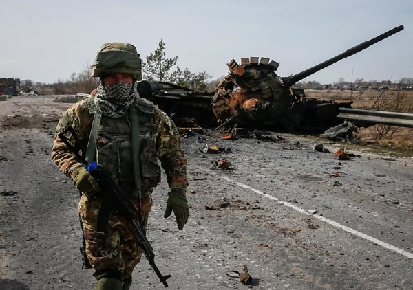 破壊したロシア軍の戦車の前を歩くウクライナ軍兵士（Ｃ）ロイター