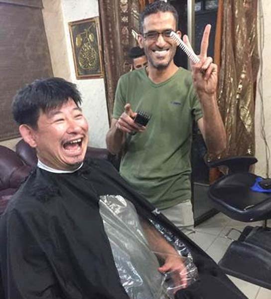 郊外の散髪店で髪を切る小田切拓氏。日本人は初めてと店主は大興奮（2019年西岸）／（写真提供）小田切拓