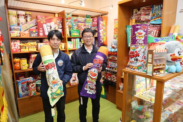 やおきんの「うまい棒」を抱きしめて。営業企画部の田中浩次さん（右）と小野貴裕さん（Ｃ）日刊ゲンダイ
